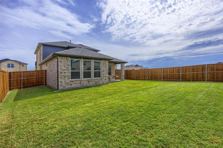 Expansive fenced backyard featuring a meticulously maintained lawn, a covered patio, and a brick exterior with multiple windows