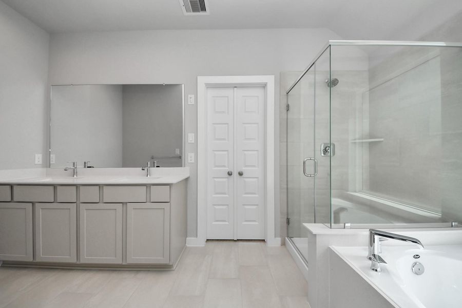 Indulge in a spa-like retreat within the confines of this primary bathroom. Delight in a spacious walk-in shower enveloped in stylish tile surround, unwind in a separate garden tub adorned with custom detailing. Sample photo of completed home with similar floor plan. Actual colors and selections may vary.