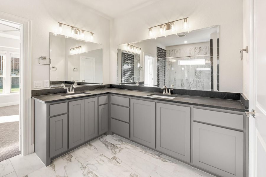 Master bathroom with dual sinks, gray L-shaped vanity, dark countertops, and marble tile floors Master bathroom with dual sinks, gray L-shaped vanity, dark countertops, and marble tile floors