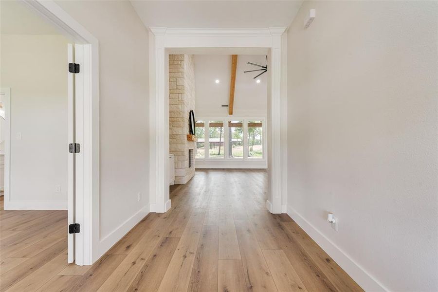 Hallway entry featuring wood-finish flooring, crisp white trim, and a clear sightline to a living space with a stone-clad fireplace, vaulted ceiling with exposed beams, and large picture windows
