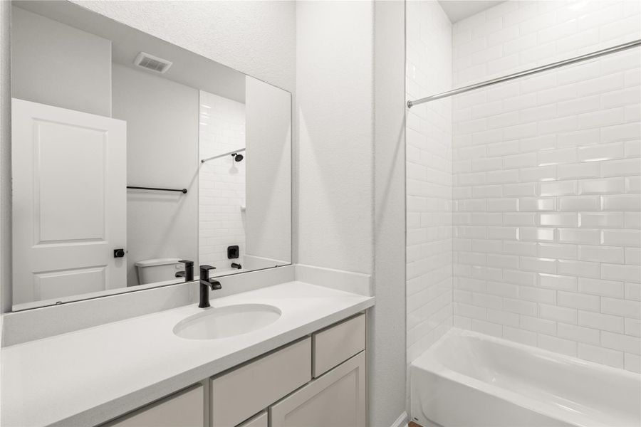 Modern bathroom showcasing a sleek vanity with a black faucet, elongated mirror, and a pristine white-tiled bathtub.