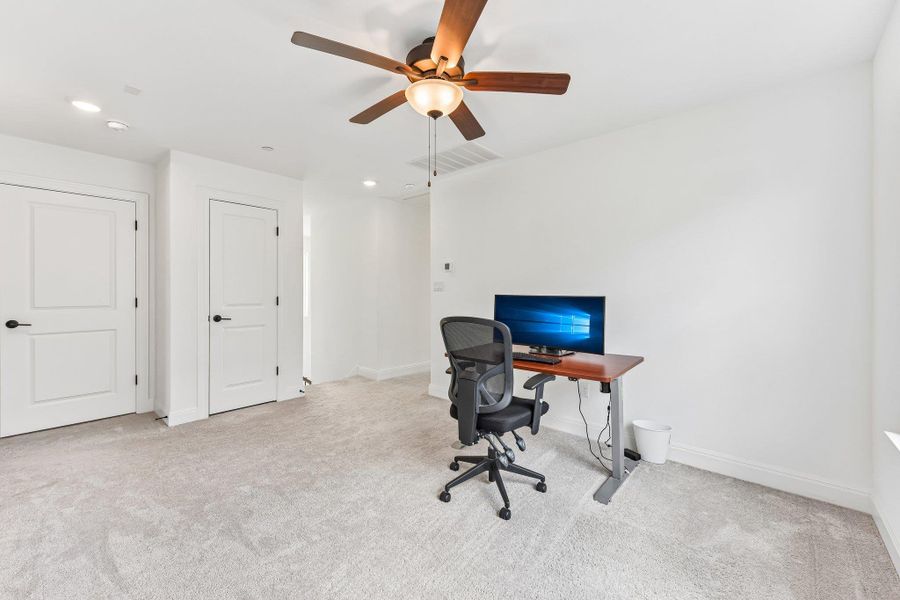 An airy office space offers plush carpeting and a modern ceiling fan with lighting.