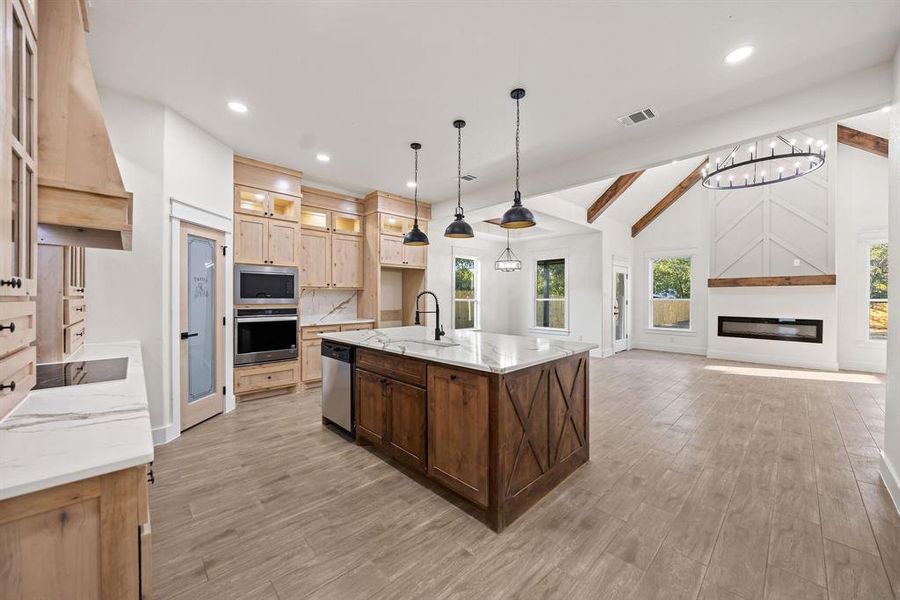 Kitchen with light stone counters, pendant lighting, glass insert cabinets, light wood finished floors, and stainless steel appliances