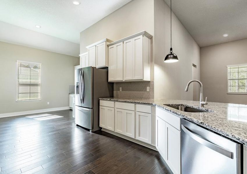 Chef-ready kitchen with granite countertops, white cabinetry, a gray backsplash, wood flooring and stainless steel appliances.