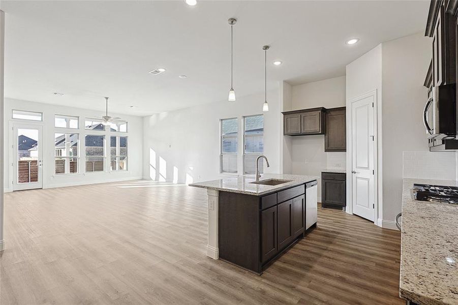 Kitchen featuring light stone counters, ceiling fan, sink, pendant lighting, and a center island with sink