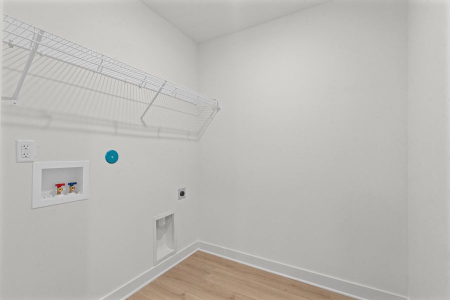 Wood-finish flooring with white baseboards, a wall-mounted wire shelf, and an integrated washer hookup