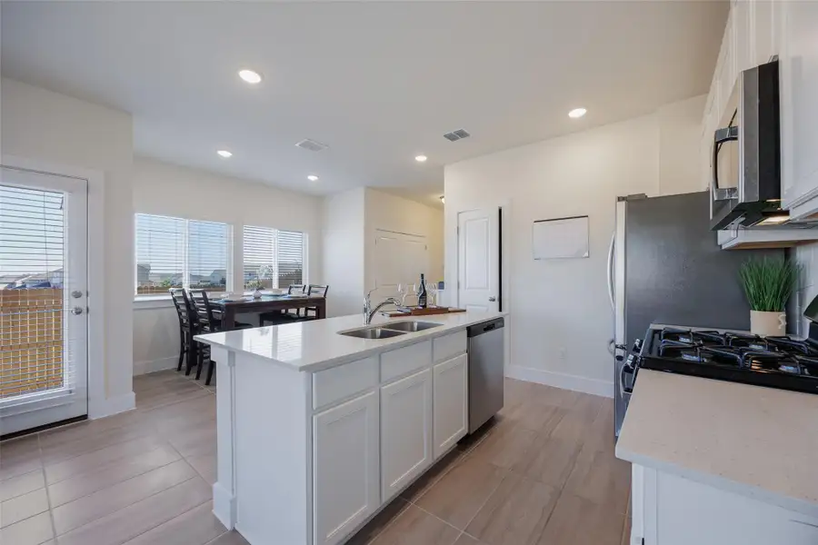 Kitchen featuring white cabinetry, an island with sink, light stone countertops, recessed lighting, and appliances with stainless steel finishes Kitchen featuring white cabinetry, an island with sink, light stone countertops, recessed lighting, and appliances with stainless steel finishes