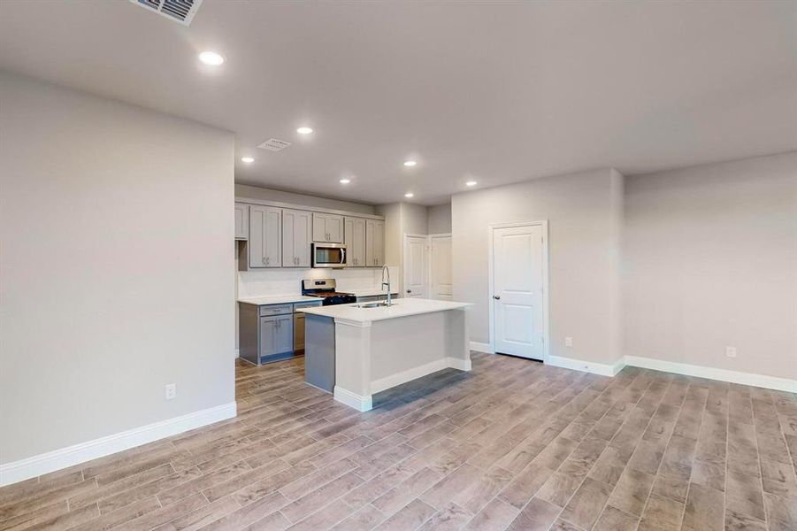 Kitchen with gray cabinets, light wood-type flooring, an island with sink, and appliances with stainless steel finishes