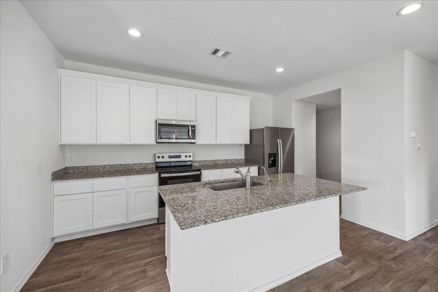 Kitchen features sleek white cabinetry, granite countertops, and stainless steel appliances, including a refrigerator and oven.