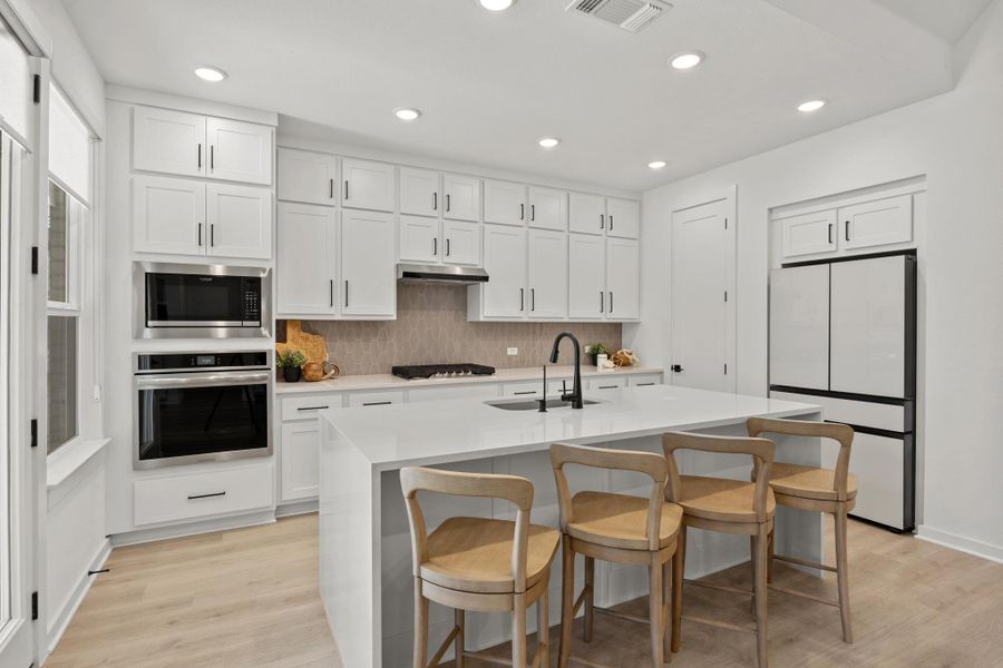 Kitchen with stainless steel appliances, a breakfast bar area, white cabinets, decorative backsplash, and light wood-style floors