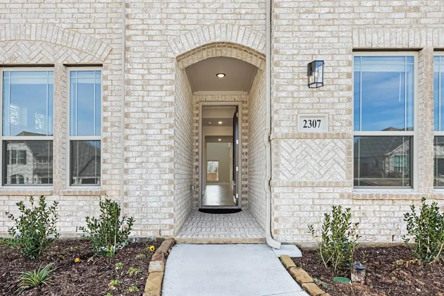 Home entrance with arched brick doorway, open front door, and address number 2307 on light brick exterior
