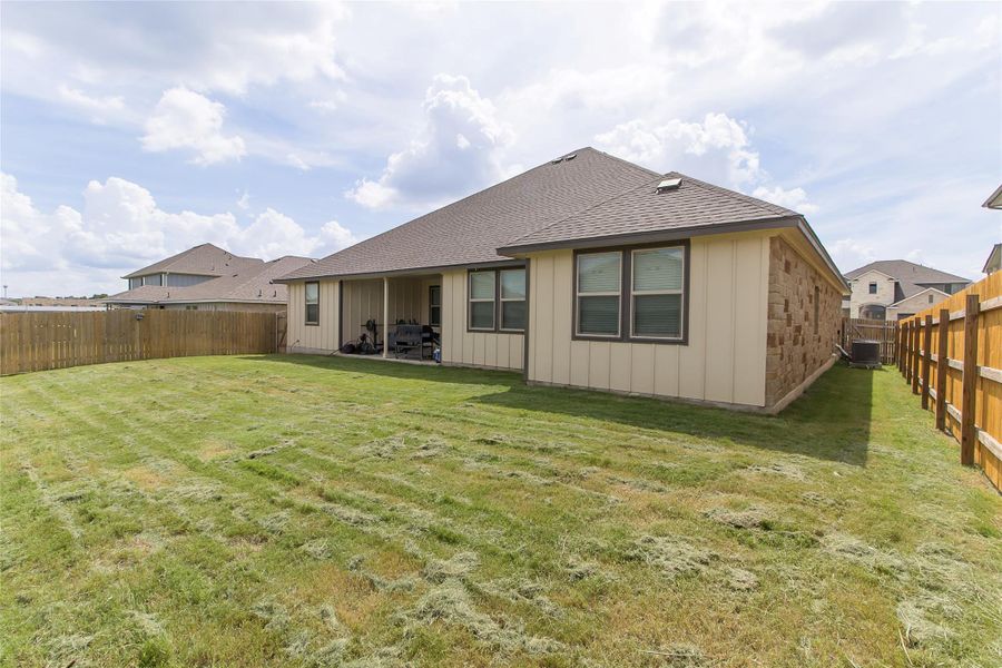 A spacious backyard with fresh-cut lawn, a covered patio, and privacy fencing.