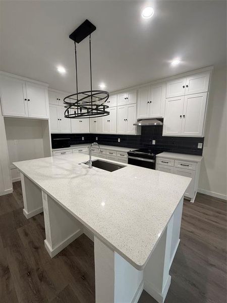 Kitchen featuring decorative backsplash, stove, range hood, white cabinetry, and a sink