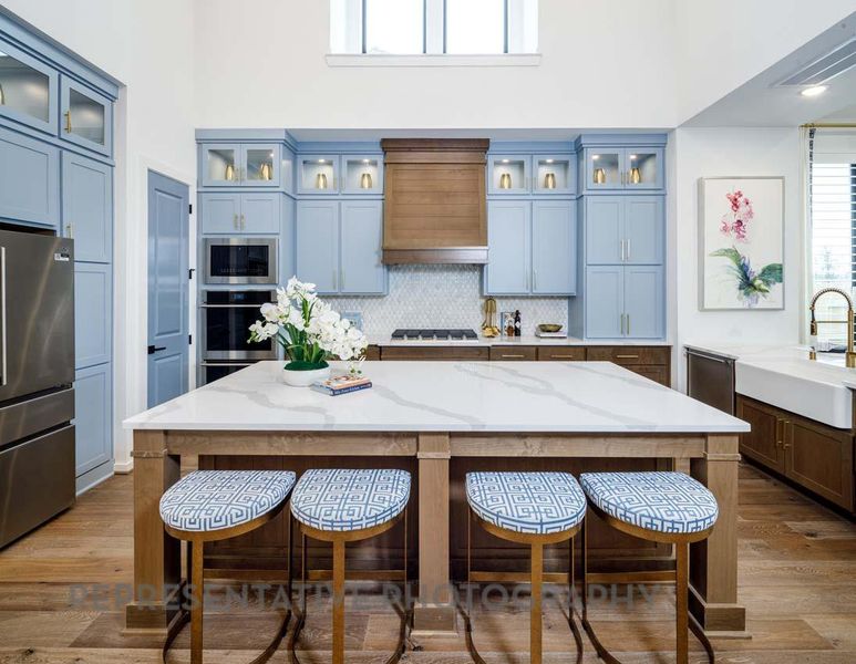 Kitchen featuring stainless steel appliances, premium range hood, a towering ceiling, a breakfast bar, and tasteful backsplash Kitchen featuring stainless steel appliances, premium range hood, a towering ceiling, a breakfast bar, and tasteful backsplash