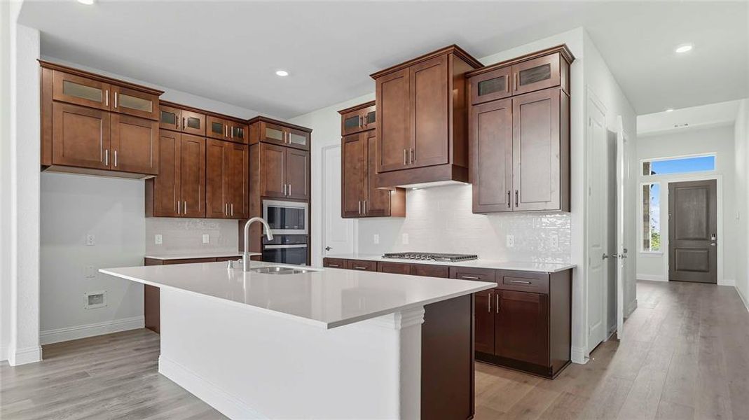 Kitchen with glass insert cabinets, an island with sink, light wood-type flooring, stainless steel appliances, and recessed lighting
