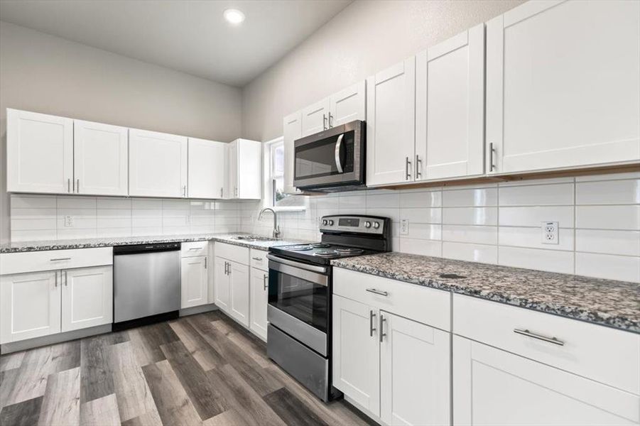 Kitchen with dark stone countertops, white cabinetry, stainless steel appliances, and dark wood-type flooring