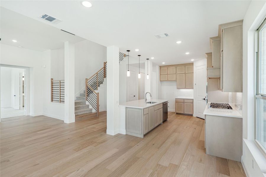 Open kitchen with center island, light wood floors, pendant lights, and staircase visible in background Open kitchen with center island, light wood floors, pendant lights, and staircase visible in background