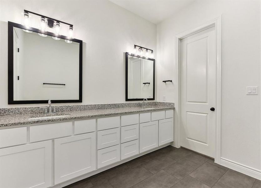 Bathroom featuring a double vanity with granite countertops, white cabinetry, and dark tiled flooring