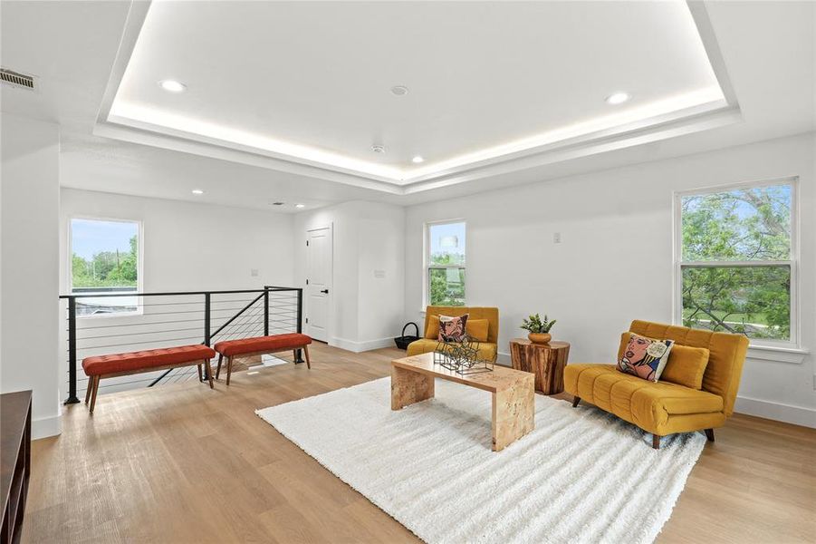 Living room with baseboards, visible vents, light wood-type flooring, and a raised ceiling