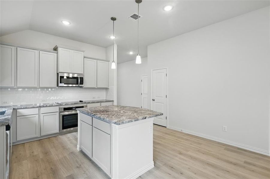 Kitchen with a center island, stainless steel appliances, pendant lighting, light stone countertops, and light wood-style flooring
