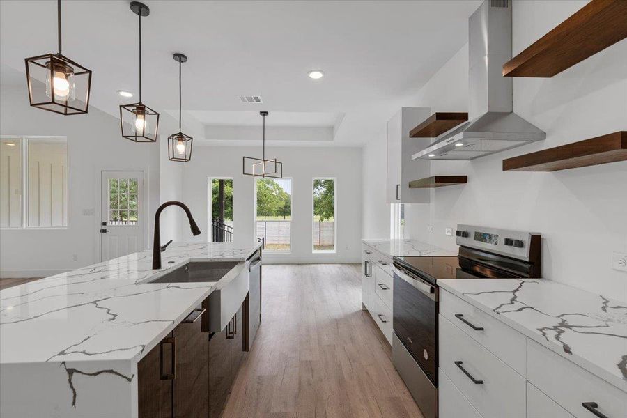 Kitchen featuring open shelves, appliances with stainless steel finishes, exhaust hood, a raised ceiling, and light wood-type flooring Kitchen featuring open shelves, appliances with stainless steel finishes, exhaust hood, a raised ceiling, and light wood-type flooring