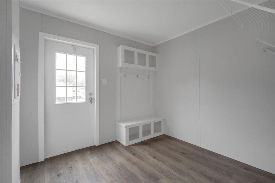 Entryway featuring a six-pane windowed door, built-in storage bench with open compartments, upper cubby storage, coat hooks, and wood-finish flooring