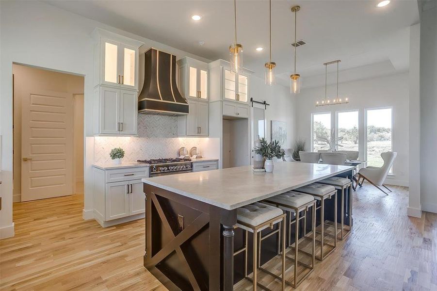 Kitchen with light hardwood / wood-style floors, white cabinetry, hanging light fixtures, a kitchen island, and custom range hood