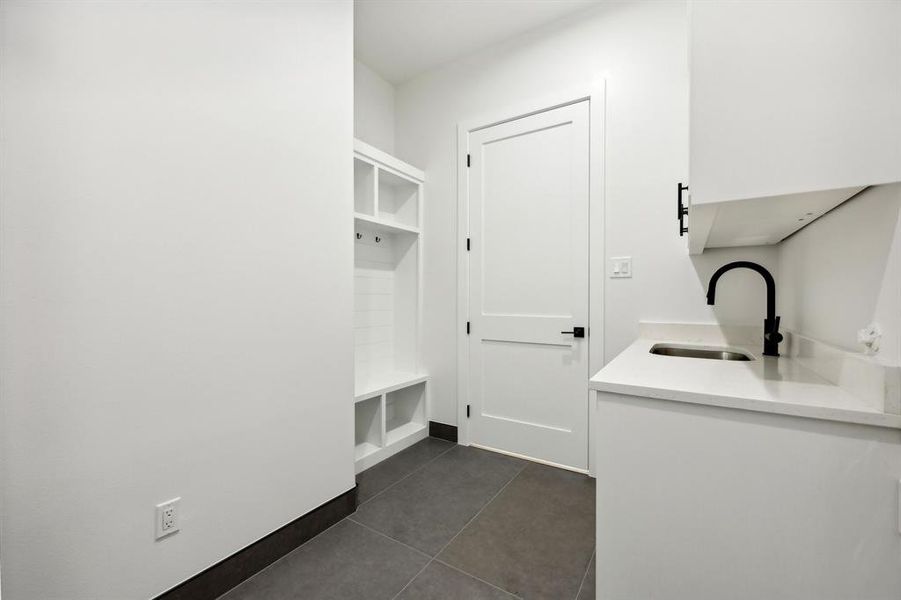 Clothes washing area with dark tile patterned flooring and sink