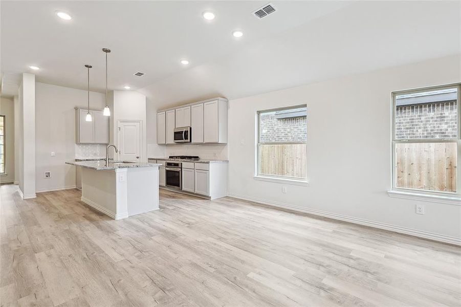 Kitchen featuring light wood-type flooring, a kitchen island with sink, stainless steel appliances, pendant lighting, and sink