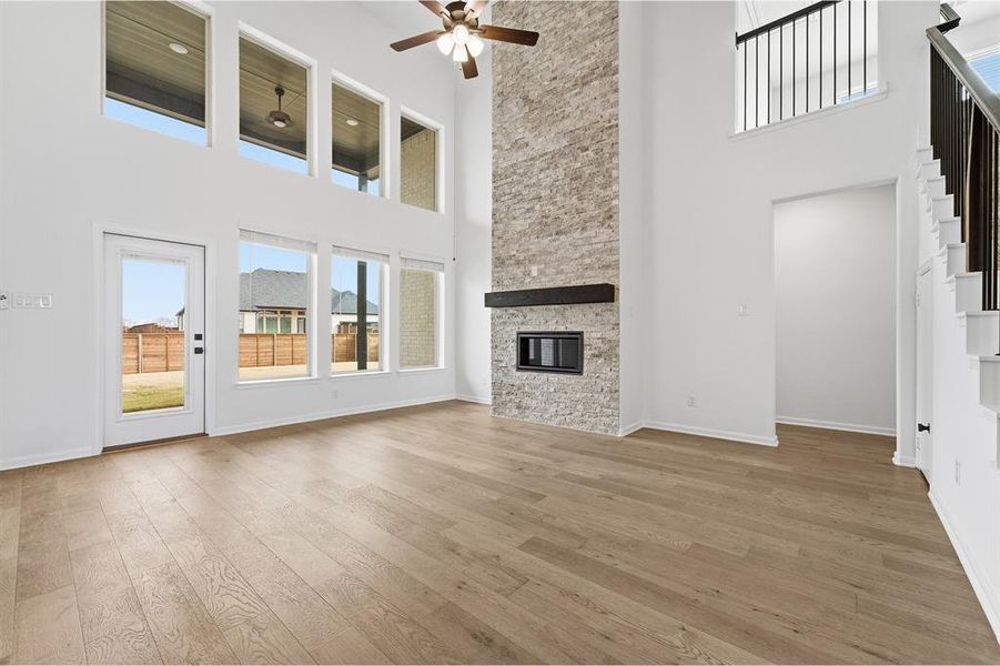 Two-story living area with wood-finish flooring, a stone-clad fireplace featuring a dark wood mantle, and multiple large windows