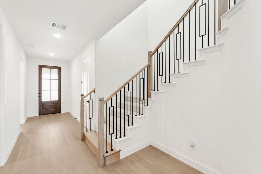 Entryway with wood staircase, black iron balusters, light hardwood floors, and wood front door with glass panels.