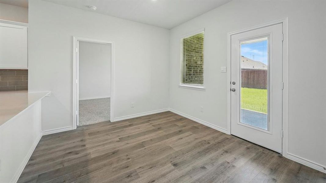 Bright interior space featuring wood-finish flooring, a contemporary white door with a clear pane, and a functional window with blinds