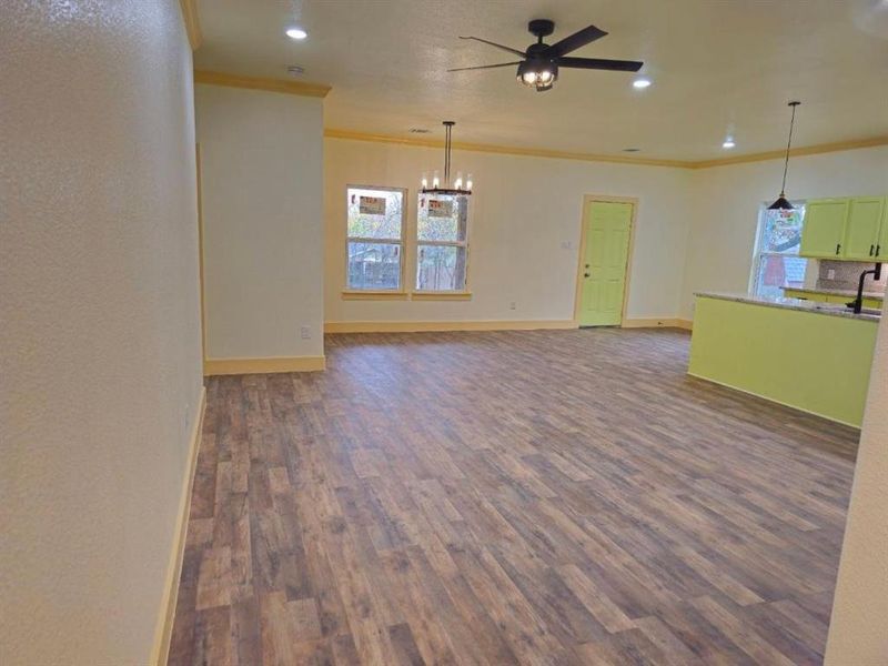 Unfurnished living room featuring ceiling fan with notable chandelier, dark hardwood / wood-style flooring, ornamental molding, and sink