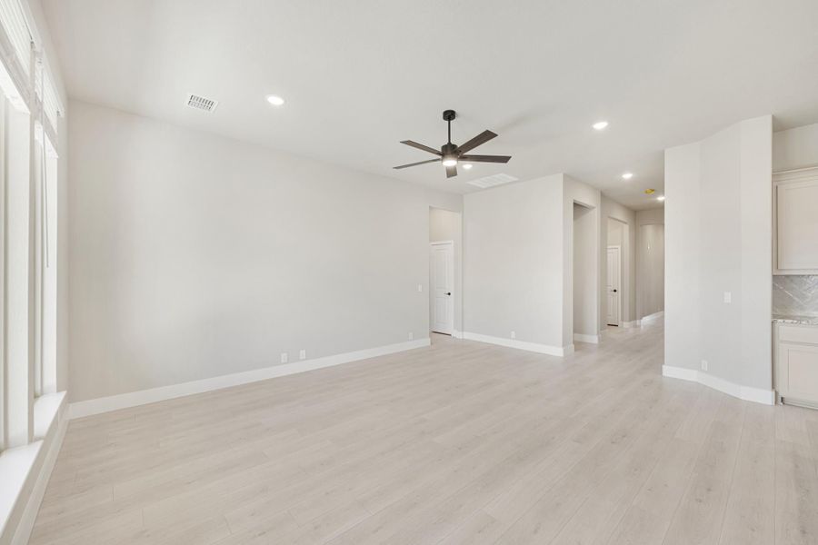 Open living area with light wood floors, white walls, ceiling fan, and recessed lighting