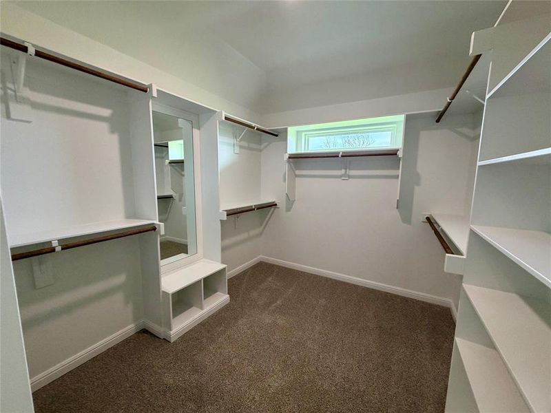 Spacious walk-in closet featuring built-in shelving, hanging rods, an integrated mirror, and a window for natural light
