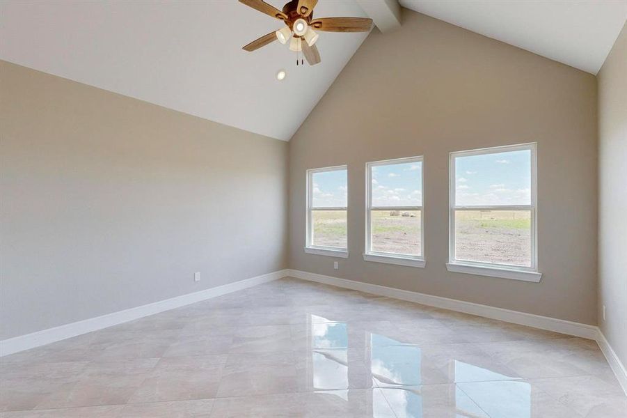 Empty room featuring beamed ceiling, light tile patterned floors, ceiling fan, and plenty of natural light