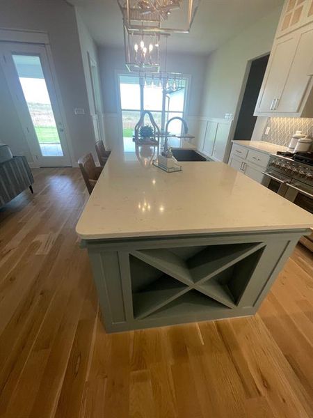 Kitchen with a sink, range with two ovens, an island with sink, white cabinetry, and wood finished floors Kitchen with a sink, range with two ovens, an island with sink, white cabinetry, and wood finished floors