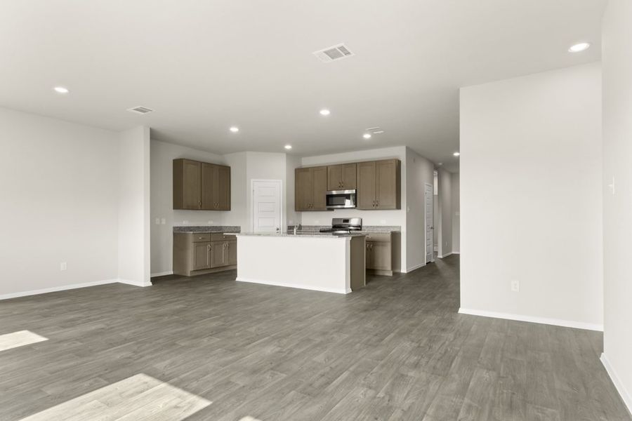 Image of a living room with dark vinyl flooring, cream walls, and a kitchen in the corner