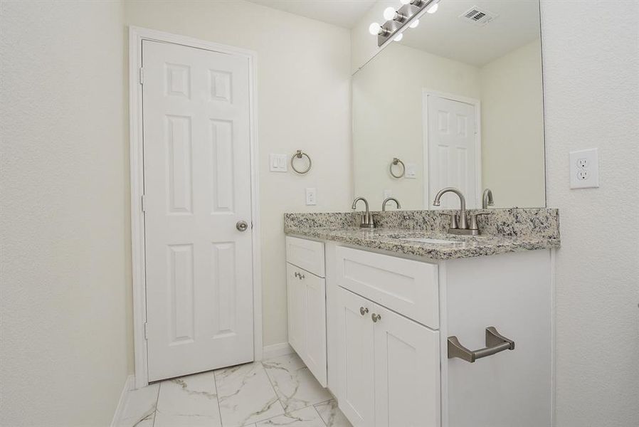 A clean, modern bathroom interior featuring a double sink vanity with granite countertop, large mirror, and tiled floor.