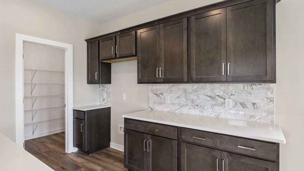 Kitchen with dark cabinetry, quartz countertops, and tile backsplash and pantry Kitchen with dark cabinetry, quartz countertops, and tile backsplash and pantry