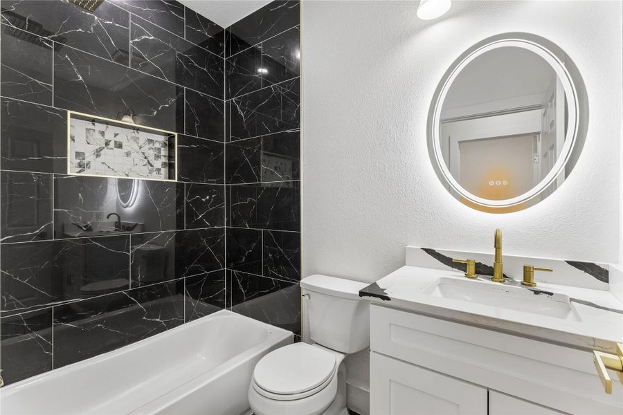 Modern bath boasts striking black marble-look tiling and a sleek, illuminated vanity.