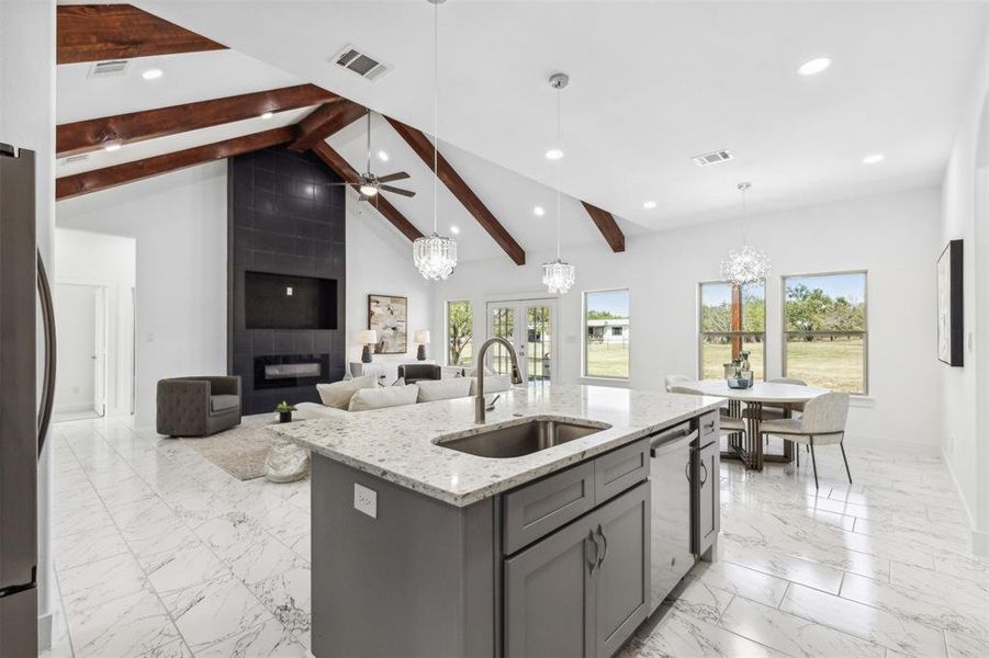 Kitchen featuring ceiling fan with notable chandelier, light tile patterned floors, beamed ceiling, a tile fireplace, and sink