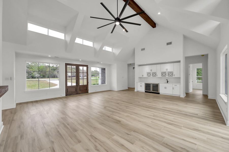 Another view of the expansive living area highlighting the architectural beam detail, oversized modern ceiling fan, and the built-in wet bar area.