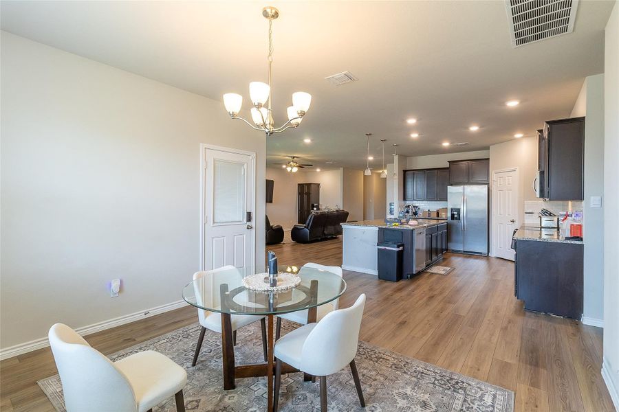 An open-concept living space integrates a dining area, kitchen, and living room under recessed and chandelier lighting.