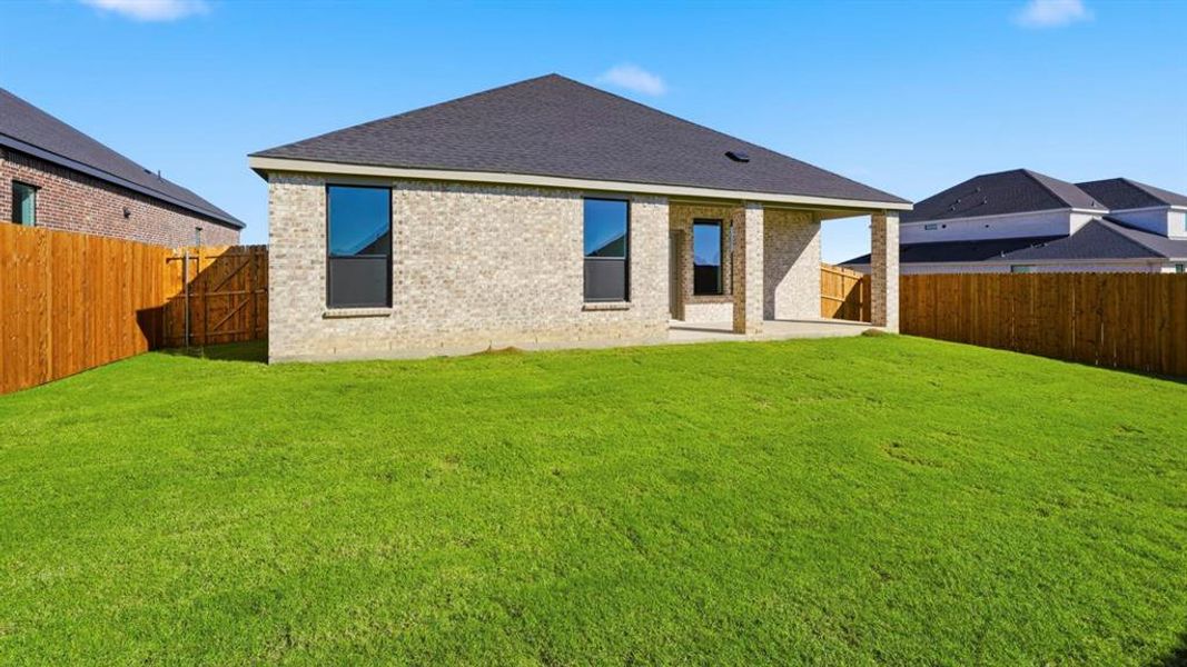Rear view of property featuring brick siding, a patio area, roof with shingles, and a fenced backyard