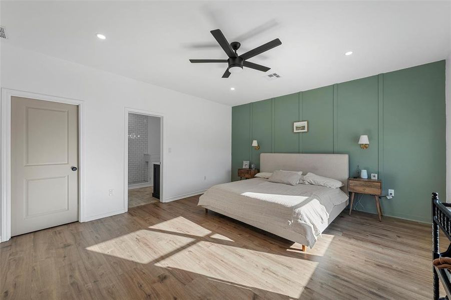 Bedroom featuring light wood-style floors, connected bathroom, a ceiling fan, recessed lighting, and a decorative wall
