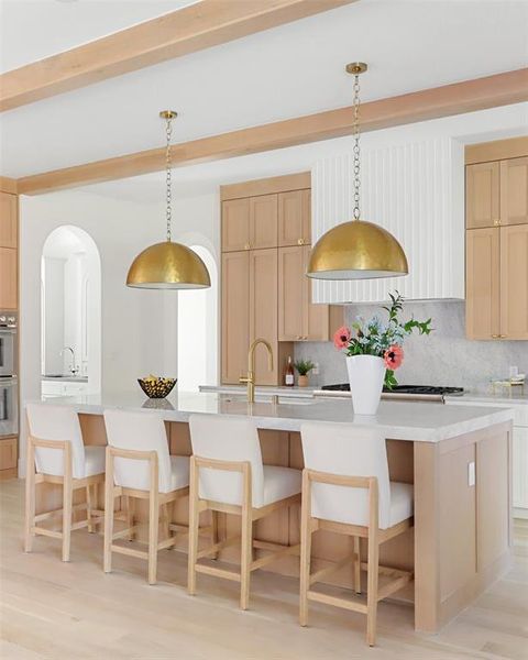 Kitchen featuring pendant lighting, backsplash, light hardwood / wood-style flooring, and an island with sink