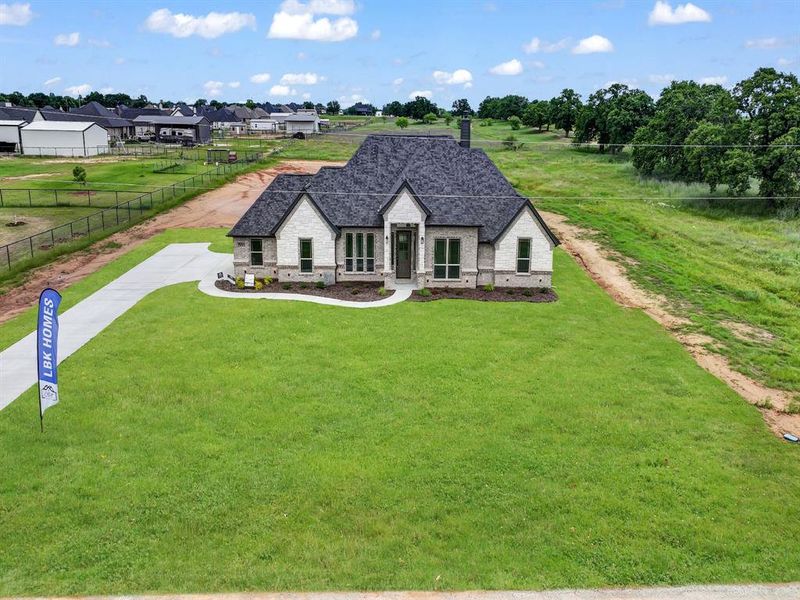 French country style house with stone siding, roof with shingles, driveway, and brick siding