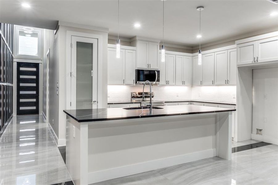 Kitchen with white cabinetry, decorative light fixtures, an island with sink, and sink