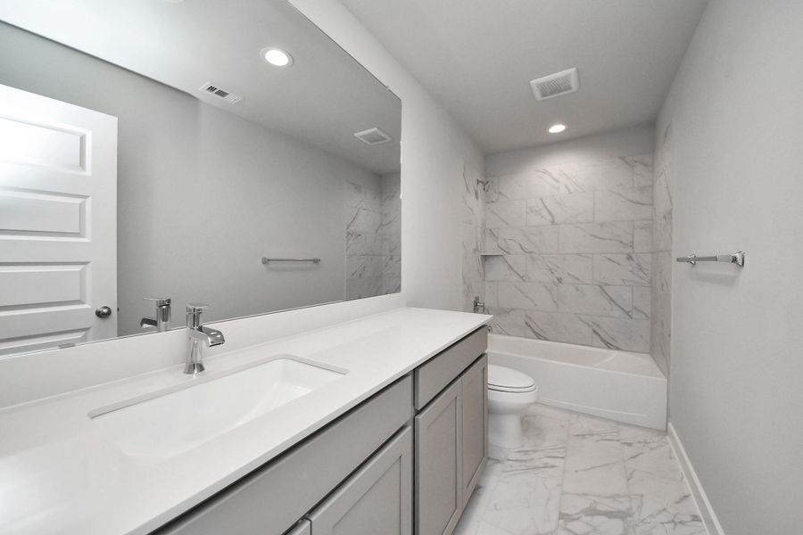 Secondary bath features tile flooring, bath/shower combo with tile surround, light stained wood cabinets, beautiful light countertop. Sample photo of completed home with similar floor plan. Actual colors and selections may vary.